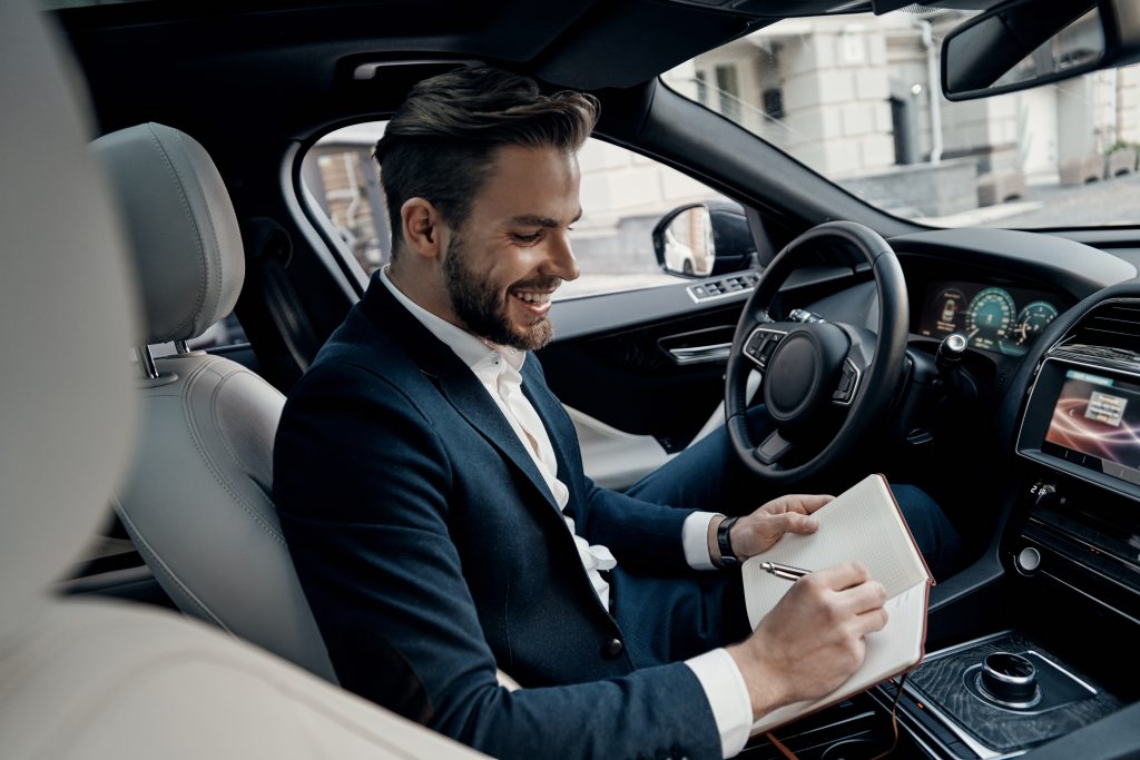 and then i am going to meet with... handsome young man in full suit writing something down in personal organizer and smiling while sitting inside of the car