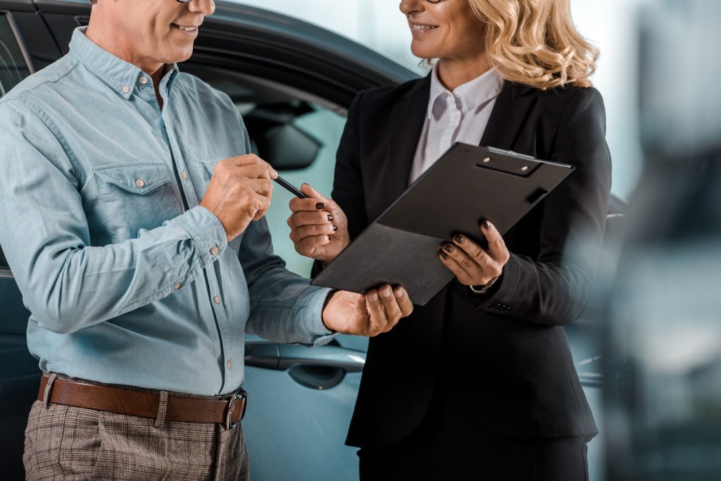 cropped shot of adult customer and female car dealer with contract standing at showroom