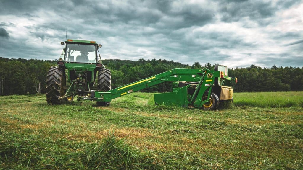 Groene tractor met maaier op landbouwveld tijdens bewolkte dag